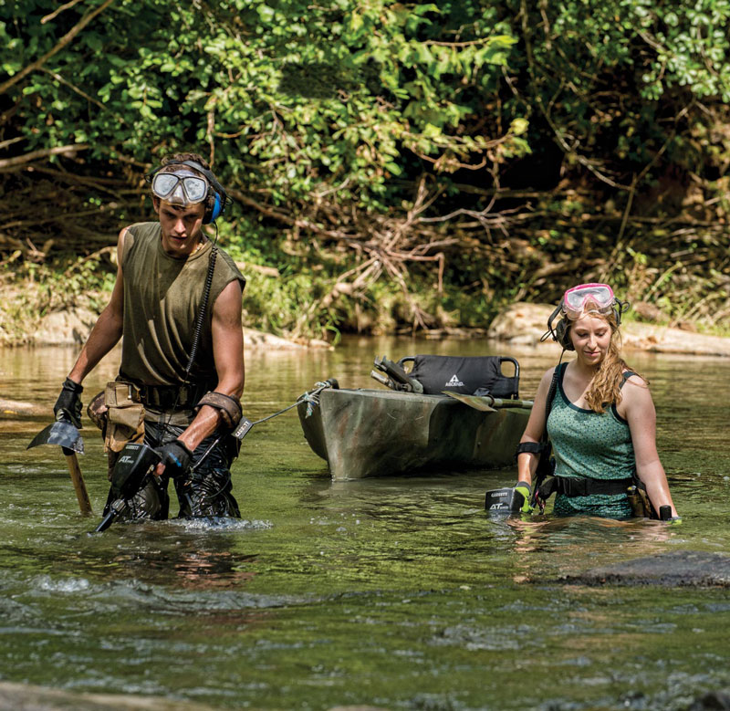 Man and woman in a stream with Garrett AT Pro metal detectors searching for treasure.