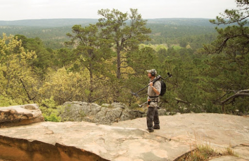 A detectorist on a rocky mountain overlooking a valley.